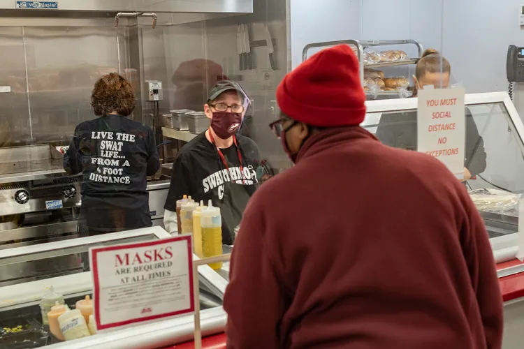 Person wearing mask stands behind plexiglass and takes order from customer at grill