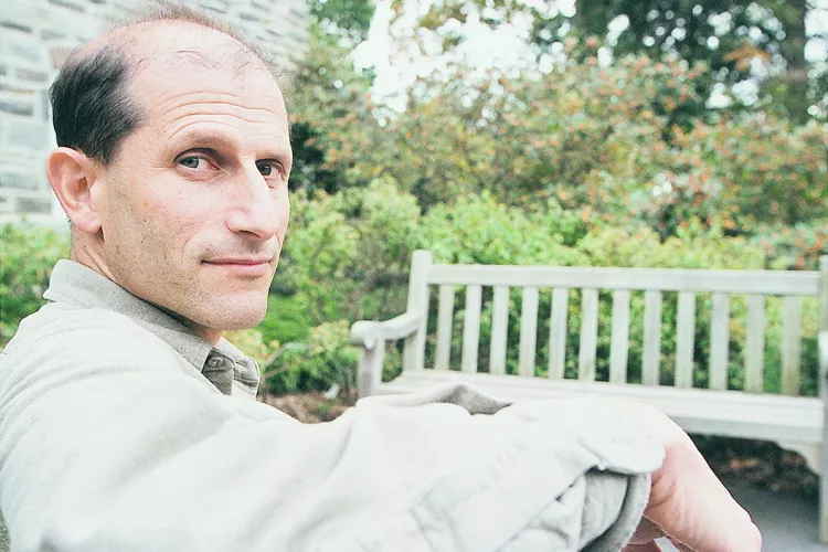 Man sitting in bench wearing beige shirt looks back at camera