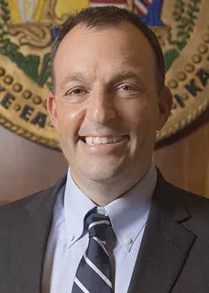 Portrait of Josh Green smiling in front of state seal of Hawaii