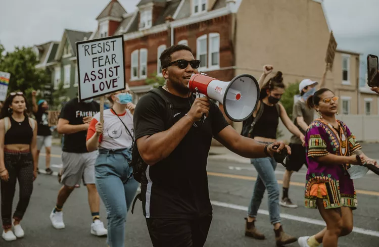 Protestor with bullhorn in foreground, surrounded by other with Black Lives Matter signs.