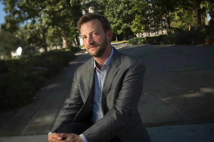 Man in suit sits on steps in shade with building in background