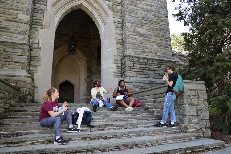 Students sit on steps of bell tower and eat lunch