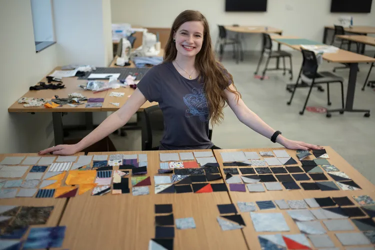 Student sits at table with clothing scraps for quilt