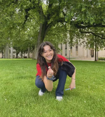 Liv crouching on a green lawn and holding up a mushroom