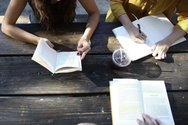 open books on a table with hands taking notes