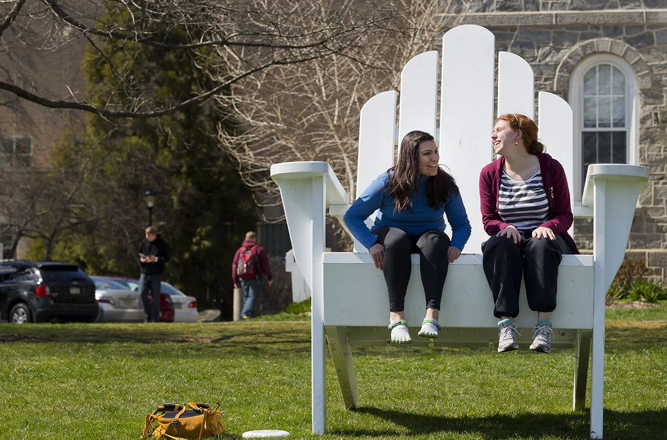 Two Swarthmore students sit together and chat on the big chair.