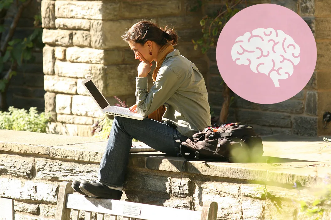 Person sits and looks at laptop outdoors. Pink circle featuring a cartoon brain in upper right corner.