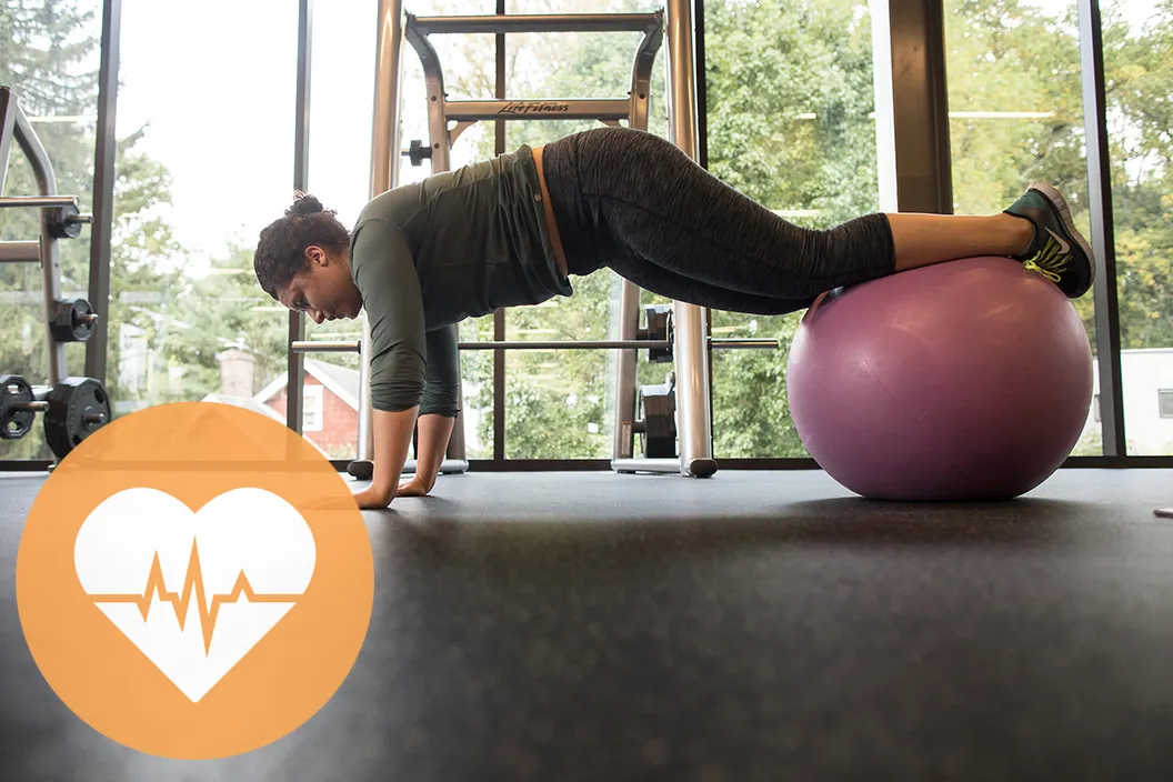 Person works out with exercise ball. Orange circle featuring a heartbeat in lower left corner