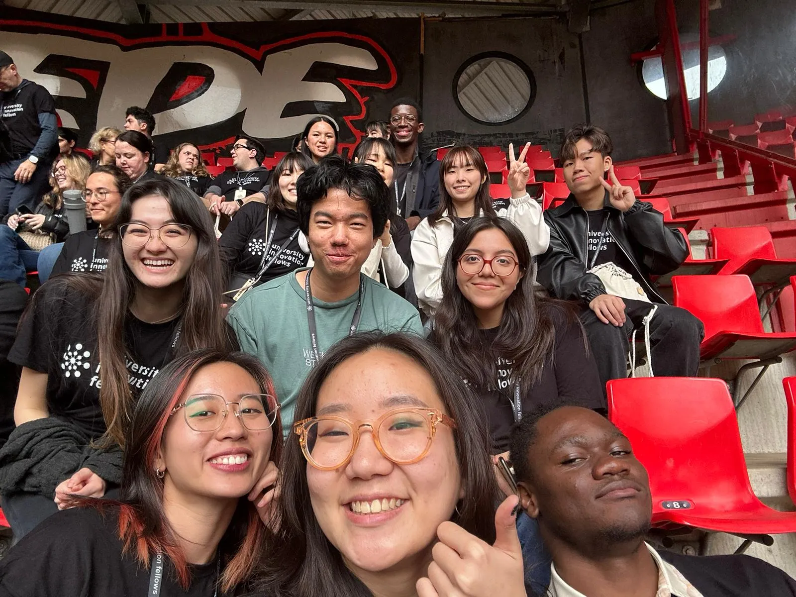 A selfie The UIF 24-25 Cohort at the first day of the meet-up in a stadium bleachers with other fellows from around the world