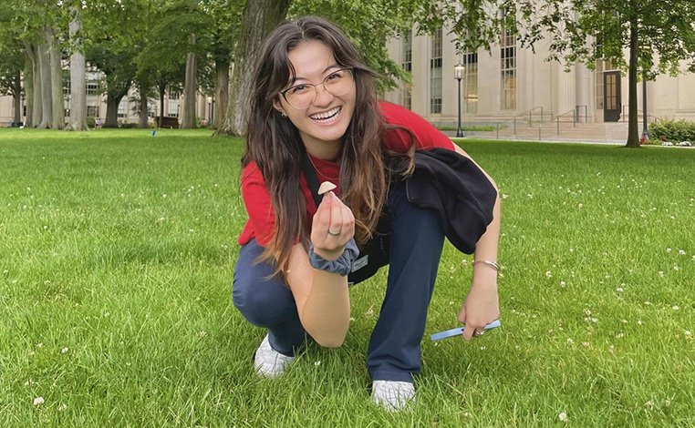 Liv Medeiros-Sakimoto crouching on a lawn and holding up a mushroom