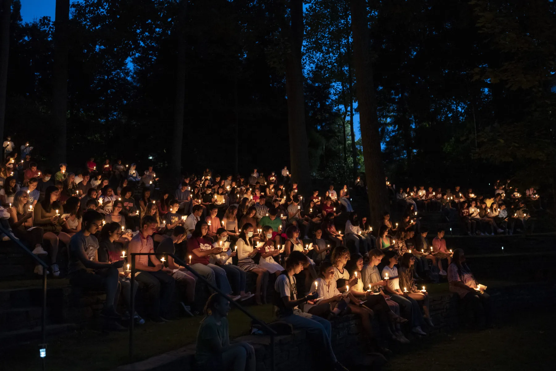 Large group of students sitting in the college's amphitheater holding candles at night time collection.