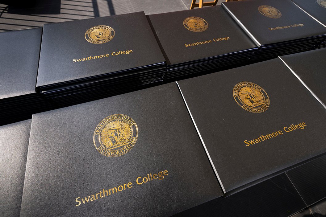 Table full of black diploma holders with "Swarthmore College" and seal