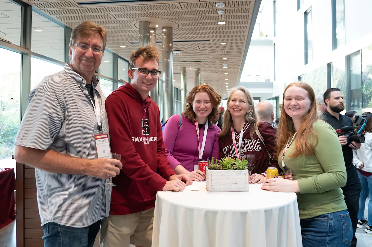 Gathered around a high-top table in Singer Hall, a group of five people smile at the camera. 