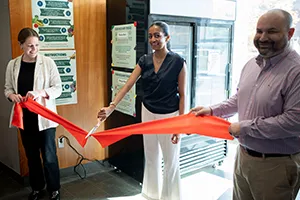 Person with large pair of scissors cuts red ribbon at ceremony