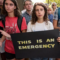 Student holds sign that says, "This is an emergency"