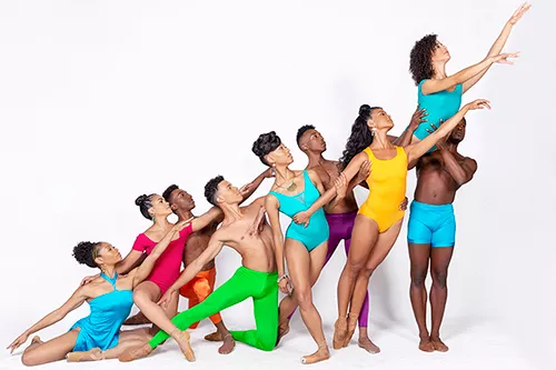 Dance troupe wearing bright pastels poses in front of white background